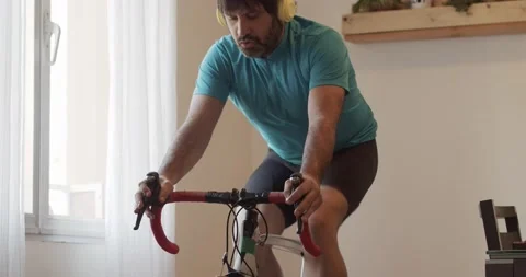 Man doing exercise bike at home while listening to music Stock Footage 145908098