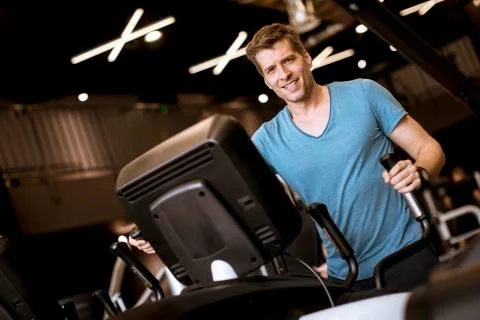 Man doing exercise on elliptical cross trainer in sport fitness gym club Stock Photos