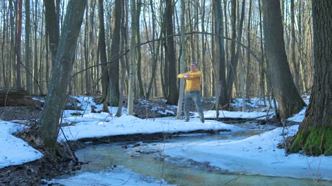 A man doing an exercise by a frozen forest stream in winter Stock Footage 346281914