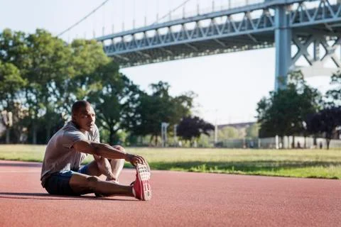 Man doing exercise in park on field against Triborough Bridge Fotos Stock