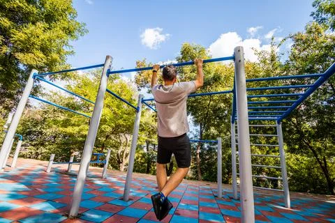 A man doing exercises on a horizontal bar in a park. Outdoor sports. Fotos Stock
