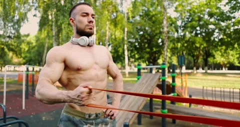 Man doing exercises with rubber band in city park.Bodybuilder training his arm Stock Footage 157452959