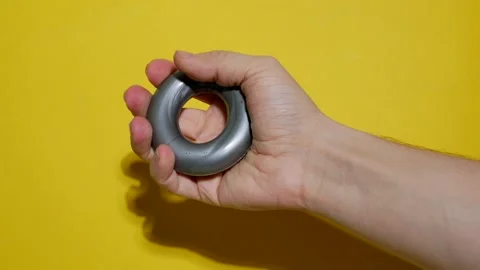 Man doing exercises squeezing rubber hand trainer on bright yellow background Stock Footage 164376512