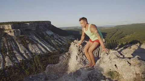 A man doing exercises on a stone on top of the mountain. Perfect musculature Stock Footage 94849482