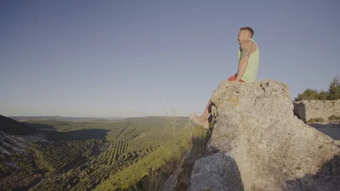 A man doing exercises on a stone on top of the mountain. Perfect musculature Stock Footage 94849484