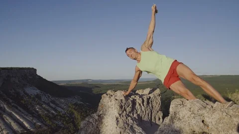 A man doing exercises on a stone on top of the mountain. Perfect musculature Stock Footage 94849510