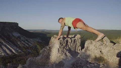 A man doing exercises on a stone on top of the mountain. Perfect musculature Stock Footage 94849549