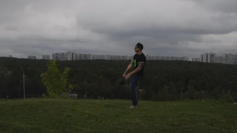 A man doing exercises with a weight on a hill overlooking the city. 120 FPS slow Stock Footage 93026776