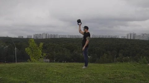 A man doing exercises with a weight on a hill overlooking the city. 60 FPS slow Stock Footage 93026803