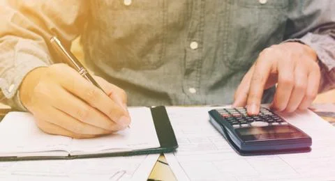 Man doing finances with using calculator and writing note in home office. Stock Photos