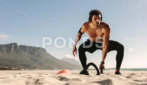 Man doing fitness training at the beach with kettlebells Stock Photos