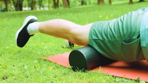 Man doing foam rolling on a mat outdoors in a park for myofascial release, self- Stock Footage 340225937