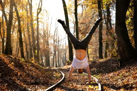 Man doing handstand on train rails with leaves on the ground during su Stock Photos
