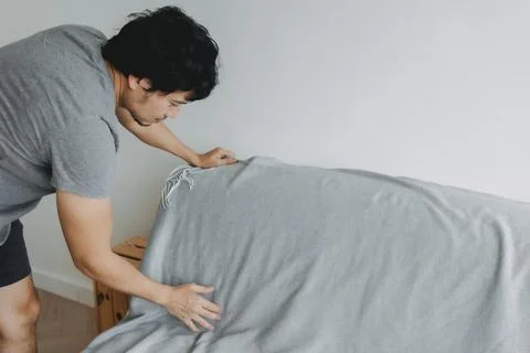 Man is doing his house work, covering the sofa with grey sheet. Stock-Fotos