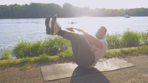 Man doing Jackknife ab muscles exercise outdoors near river Stock Footage 123332812