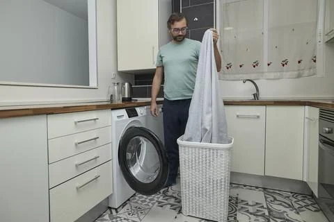 Man doing laundry at home in modern kitchen Stock Photos