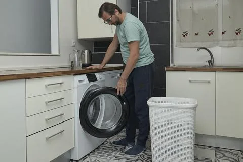 Man doing laundry at home in modern kitchen Stock Photos