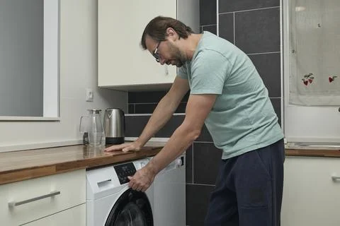 Man doing laundry at home in modern kitchen Stock Photos