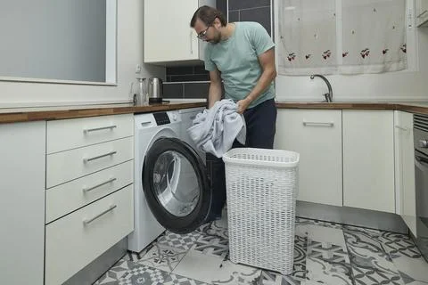 Man doing laundry at home in modern kitchen Stock Photos