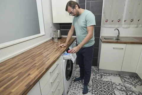 Man doing laundry at home in modern kitchen Stock Photos
