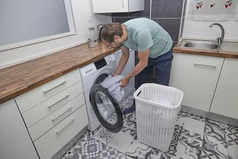 Man doing laundry at home in modern kitchen Stock Photos