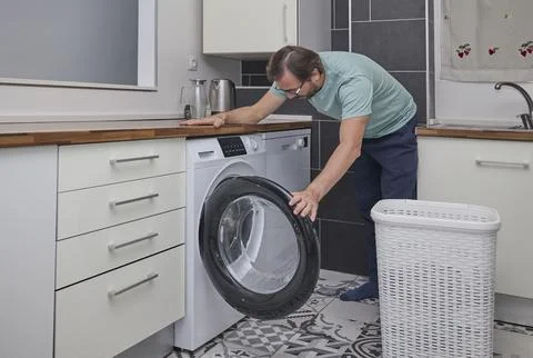 Man doing laundry at home in modern kitchen Stock Photos