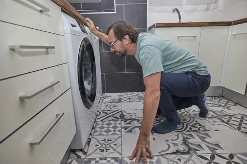 Man doing laundry at home in modern kitchen Stock Photos