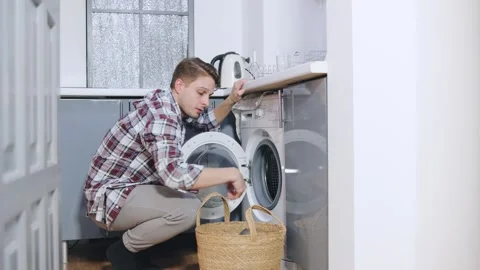 Man doing laundry at home while wearing casual clothes in a well-lit kitchen on Stock Footage 320440761
