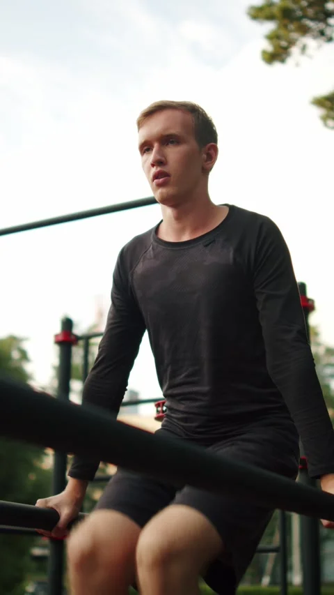 Man doing leg raises on parallel bars outdoors. Young male athlete training.. Stock-Footage 341728465
