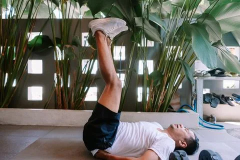 Man doing leg raises workout with tropical plants background indoor Stock Photos