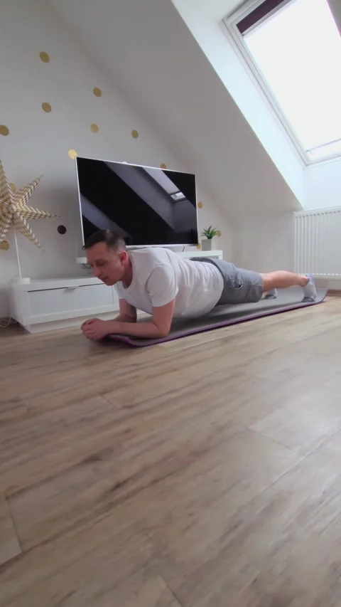 A man is doing a plank on a mat in a living room Video stock 328258195