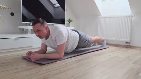 A man is doing a plank on a mat in a living room Video stock 328258525