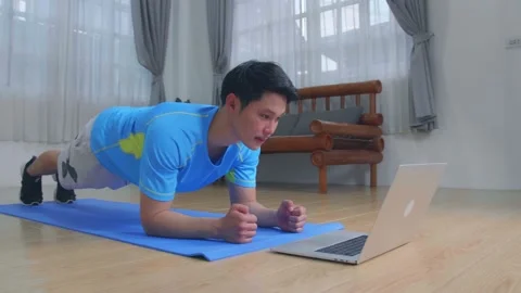 Man Doing A Plank While Watching Online Tutorial On Laptop, Exercising Video stock 153238358