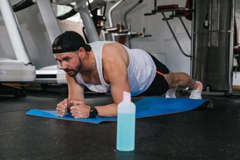 Man doing planks in the gym. Hydro alcoholic gel, coronavirus, pandemic. Stock Photos