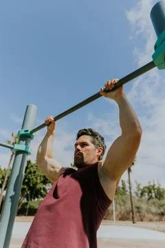 A man is doing a pull up with a high bar at an outdoor gym, vertical photo .. Stock Photos