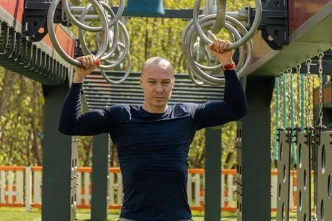 Man doing pull-ups and gymnastic ring exercises. Outdoor sports public park. Stock Photos