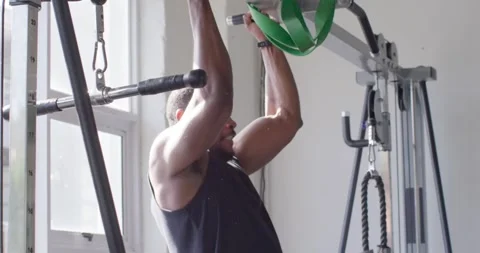 Man doing pull-ups with green band looped over bar at gym, wearing tank for Stock Footage 340675064