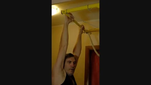 Man doing pull-ups on a wall-mounted chin-up bar at home Stock Footage 327868806