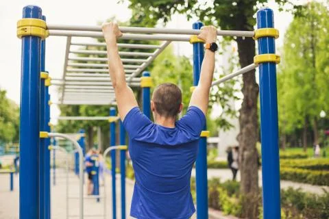 Man doing pull ups workout in the ground park. View from back. Stock Photos
