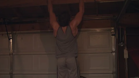 Man doing pullups on a cross beam in garage in 4k. Stock Footage 93675343