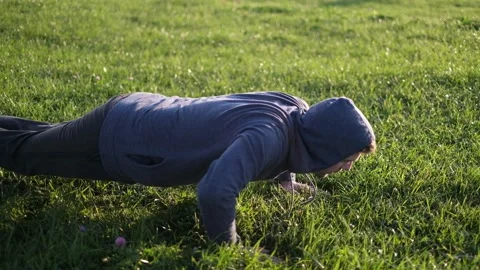 A man doing a push up in a park on green grass Stock Footage 116504916