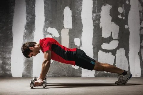 Man doing push ups on dumbbells  the wall backdrop Stock Photos