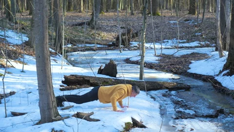 Man doing push ups on melting snow in forest during spring outdoor workout Stock Footage 334839502