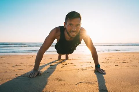 Man doing push ups or exercising on the beach during sunset. Healthy lifestyle Stock Photos