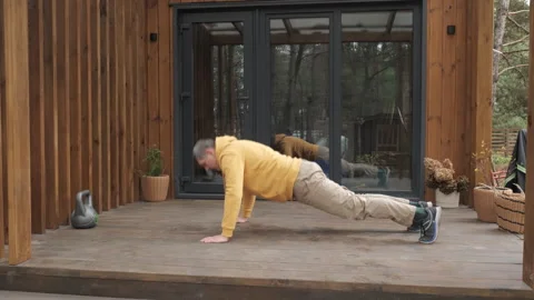 Man doing push ups on wooden terrace near modern cabin Stock Footage 336307749