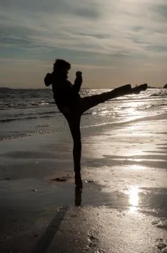 A man doing a side kick at the beach at sunrise Stock Photos