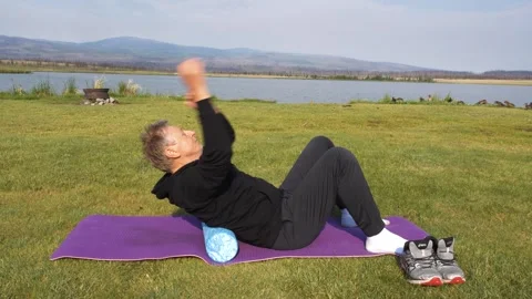 Man doing some exercisers with foam roller on a lake shore. Video stock 248942134