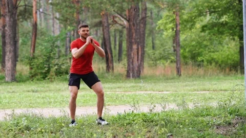 Man doing squats at the edge of the park. Video stock 146836084