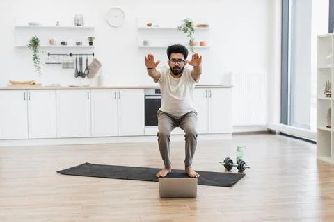 Man doing squats on mat at home while following online exercise class Foto stock