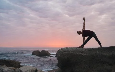Man doing the triangle pose by the ocean at dusk Foto stock